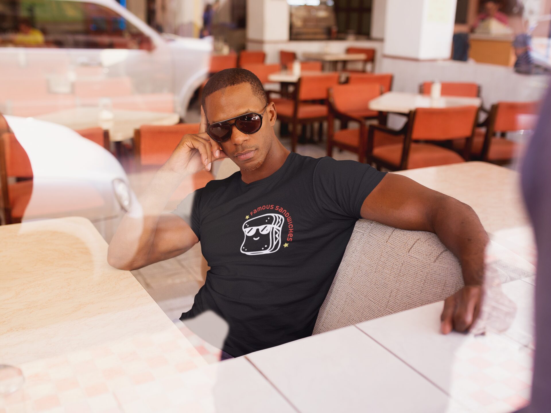 mockup-of-a-man-sitting-down-in-a-diner-restaurant-while-wearing-a-t-shirt-and-sunglasses-a14219